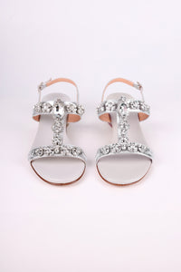 Silver low heels  sandals with decorative straps on a light pink background
