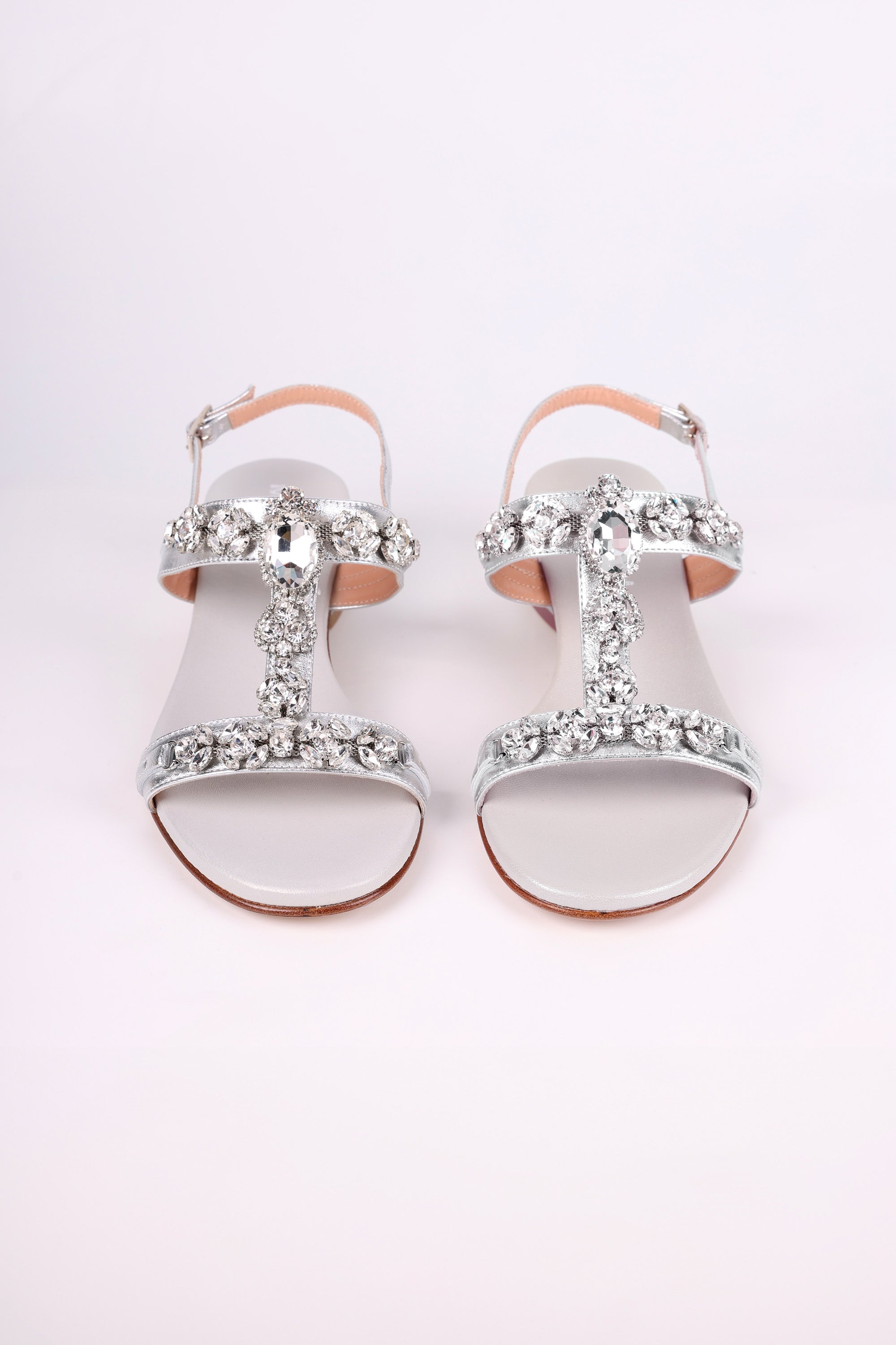 Silver low heels  sandals with decorative straps on a light pink background