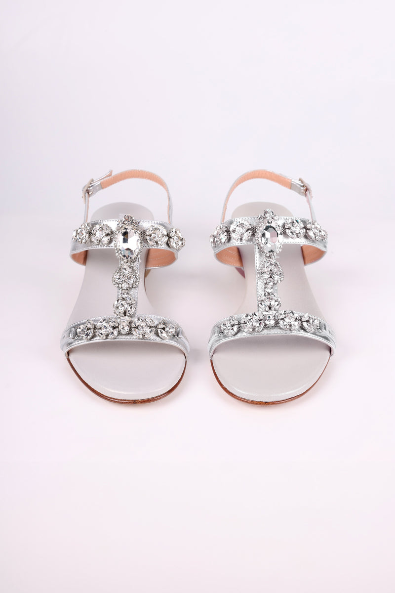 Silver low heels  sandals with decorative straps on a light pink background